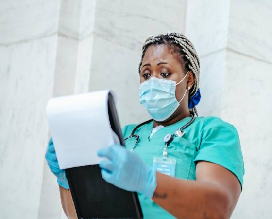 Home Attentive mature African American female medic in uniform with stethoscope and clipboard against wall at work